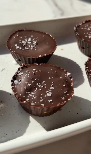 Healthy 3 ingredient dark chocolate peanut butter cups topped with flaky sea salt on a white marble surface
