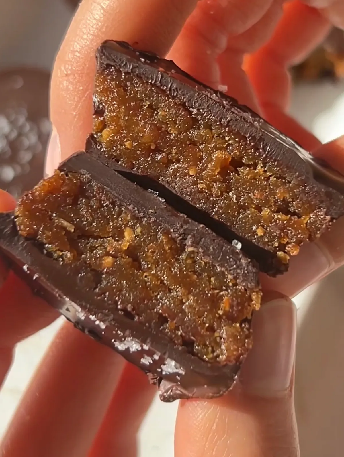 Hand holding a homemade peanut butter cup broken in half revealing a fudgy date and peanut butter filling inside a dark chocolate shell