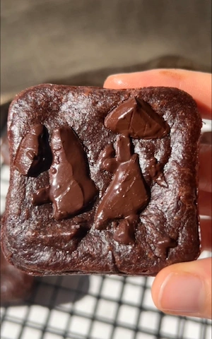 A hand holding up a single fudgy 3 ingredient banana brownie square with melted chocolate chunks on top