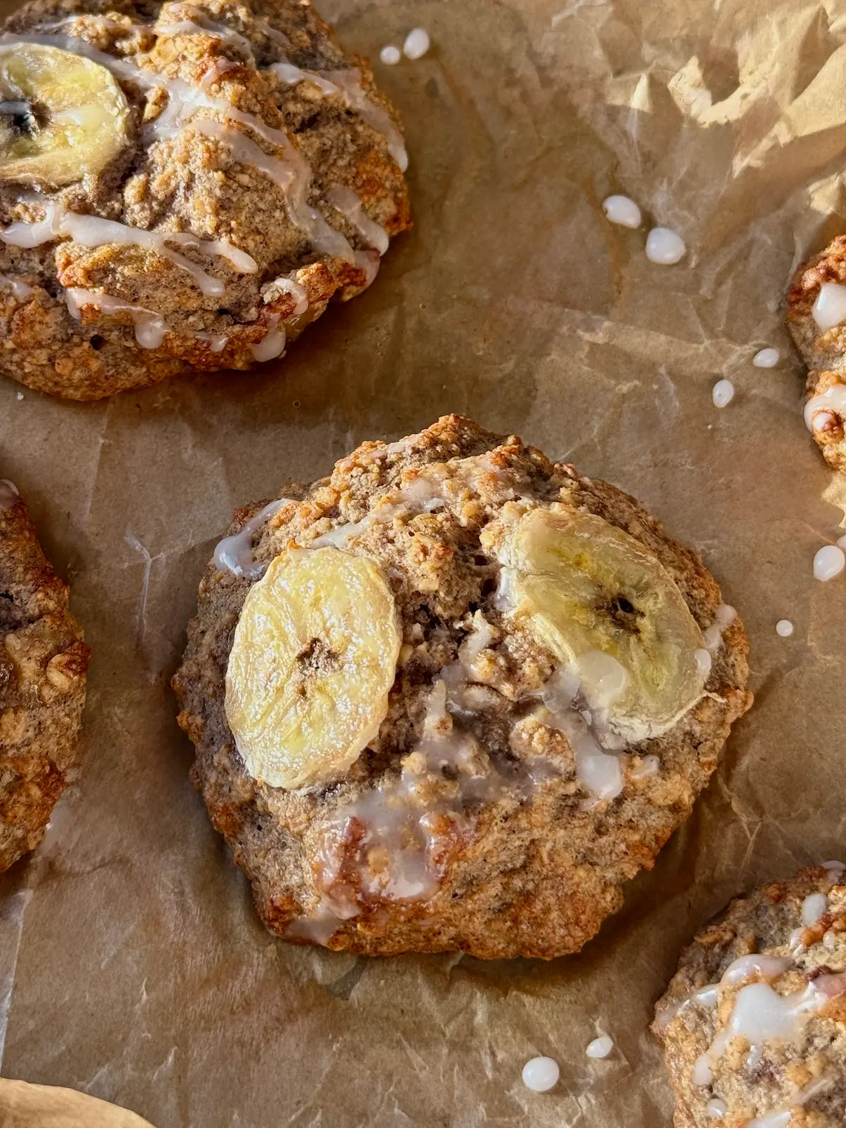 Golden baked banana fritters on parchment paper drizzled with white icing and topped with caramelised banana slices