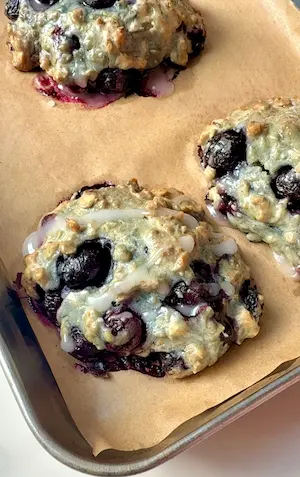 A hand holding a blueberry fritter broken open showing the jammy blueberry filling with more fritters in the background