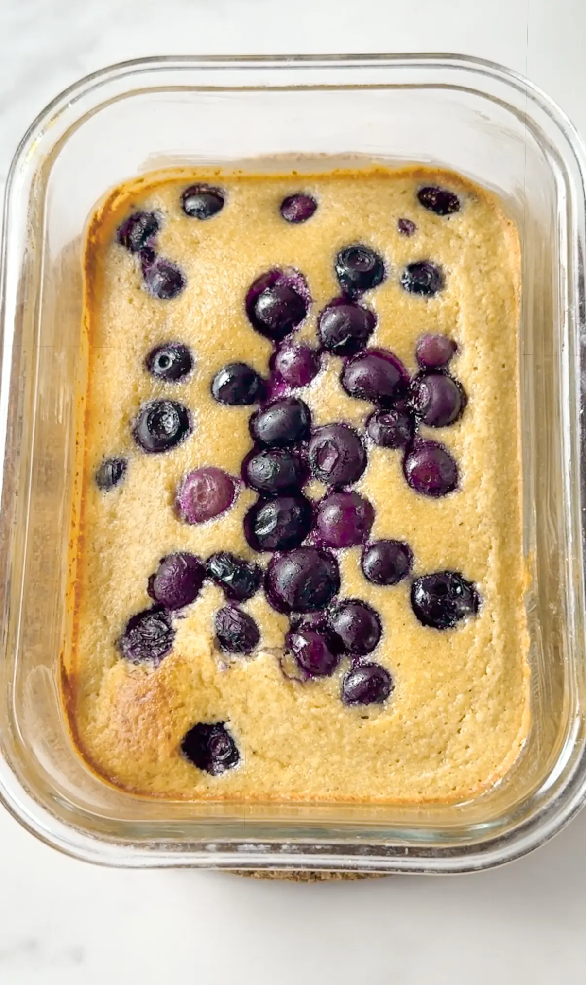 Baked blueberry muffin pancake bowl in a glass dish, topped with jammy blueberries