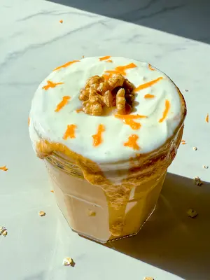 A jar of blended carrot cake overnight oats topped with a swirl of yogurt, walnut halves and thin carrot ribbons