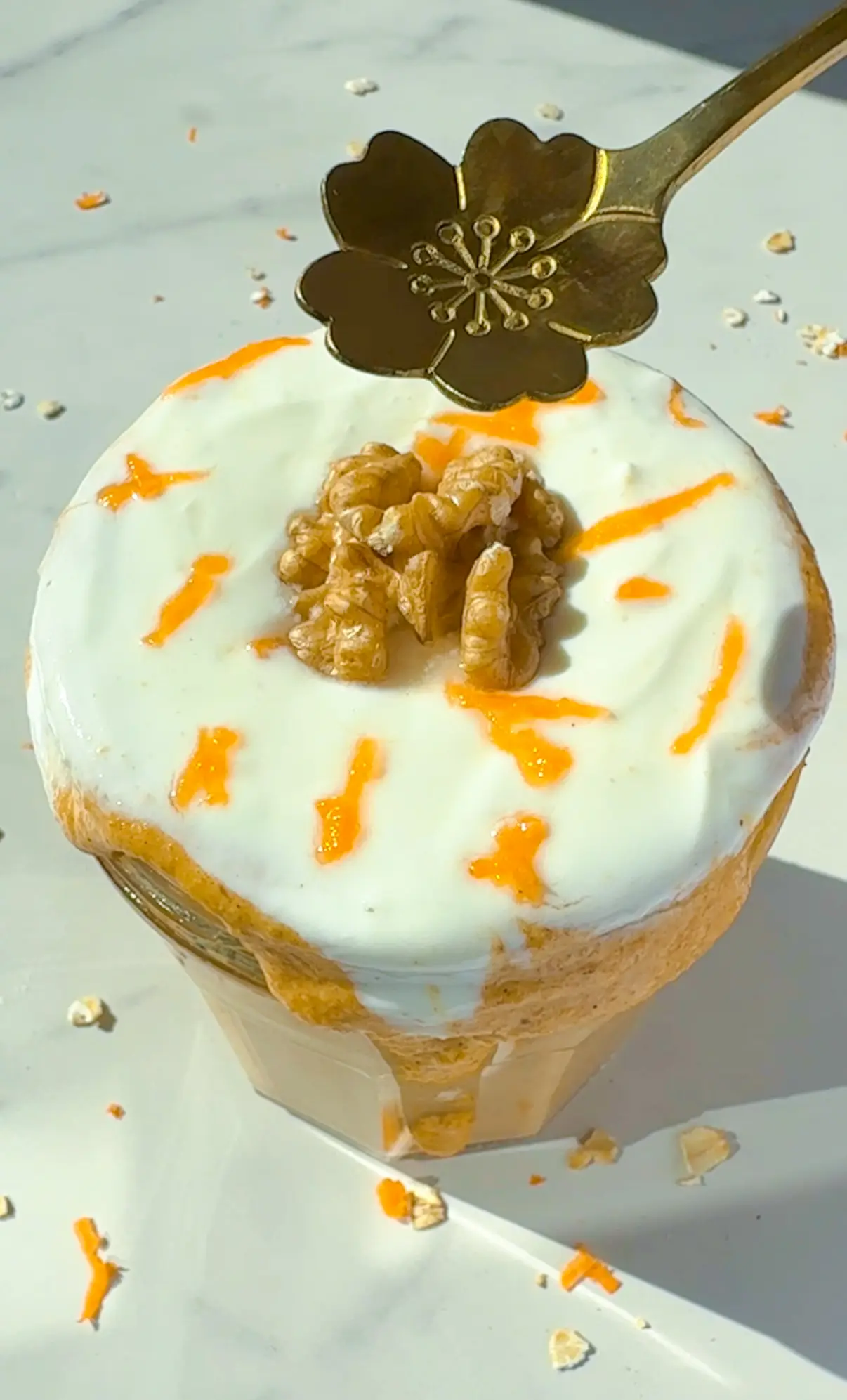 A jar of blended carrot cake overnight oats topped with a swirl of yogurt, walnut halves and thin carrot ribbons, with a gold flower-shaped spoon resting on top