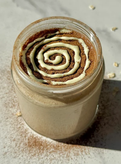 Creamy blended cinnamon roll overnight oats in a glass jar with a cinnamon drizzle on top