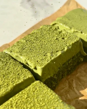A hand holding a no bake matcha ganache bar broken in half showing the chewy green matcha base and creamy bright green ganache layer