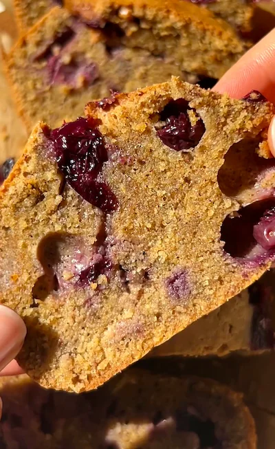 A hand holding a slice of mini blueberry olive oil loaf cake showing the golden crumb with juicy blueberries