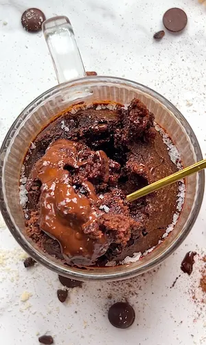 A gooey triple chocolate mug cake in a glass mug with a molten chocolate centre and chocolate chips scattered around
